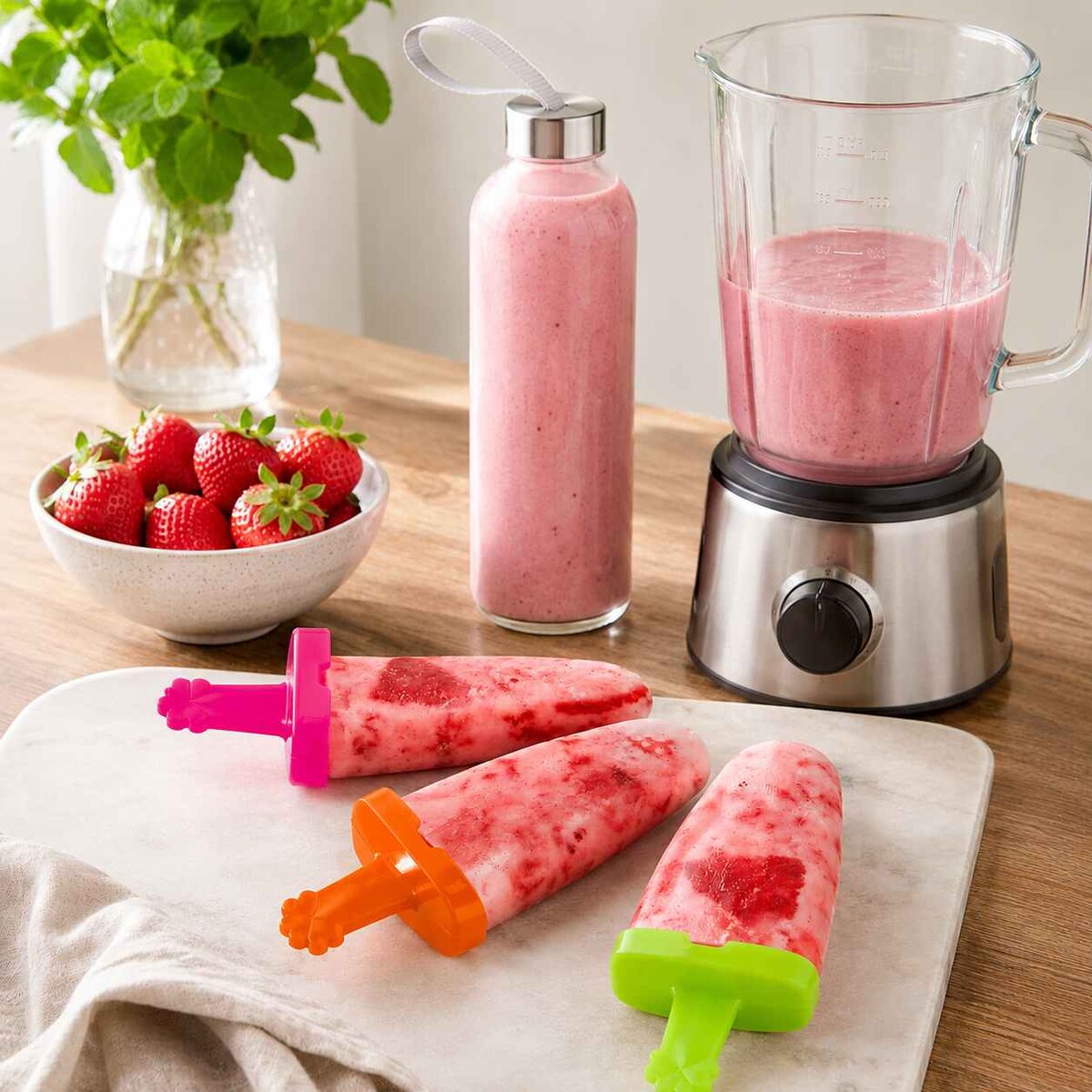 jahodové nanuky vo formách na nanuky a sklenená fľaša s jahodovým smoothie